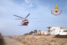 Elicottero dei Vigili del Fuoco in fase di atterraggio in una zona di campagna, con alcune case sullo sfondo