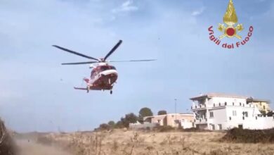 Elicottero dei Vigili del Fuoco in fase di atterraggio in una zona di campagna, con alcune case sullo sfondo