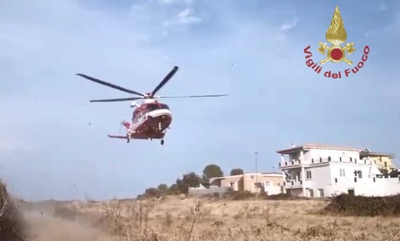 Elicottero dei Vigili del Fuoco in fase di atterraggio in una zona di campagna, con alcune case sullo sfondo