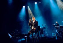 Mario Biondi in concerto sul palco, seduto al microfono sotto le luci blu