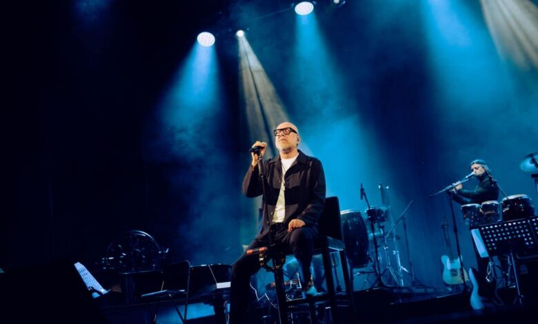 Mario Biondi in concerto sul palco, seduto al microfono sotto le luci blu