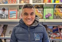 Bachis Medde sorride davanti agli scaffali della sua libreria
