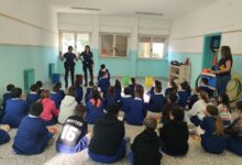 Agenti della Polizia locale di Sassari parlano a una classe di bambini seduti sul pavimento