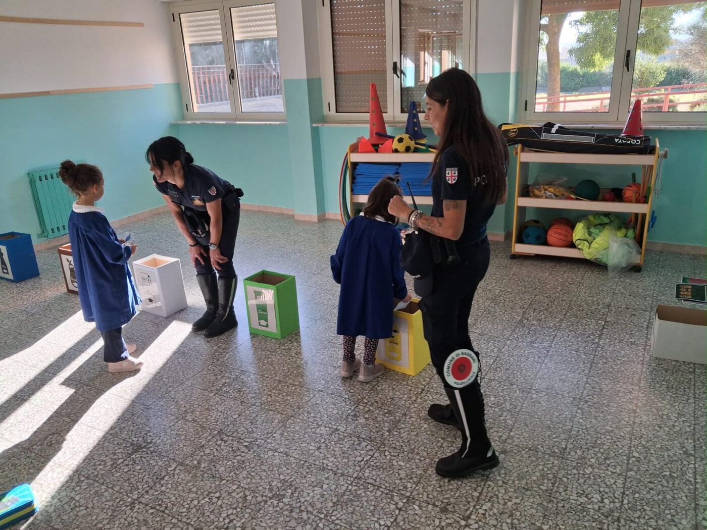 Due agenti della Polizia locale guidano due bambine in un gioco sulla raccolta differenziata